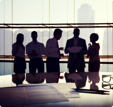 shutterstock_174966596-1 A group of people standing around a table.